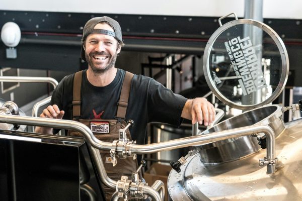 Happy brewer in a craft brewery standing near stainless steel equipment.