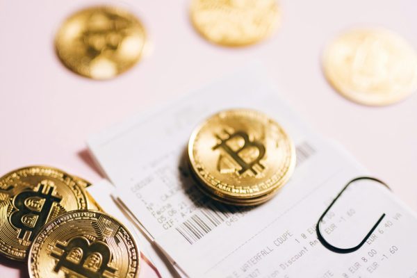 Close-up of Bitcoin coins and financial receipts on a pink background.